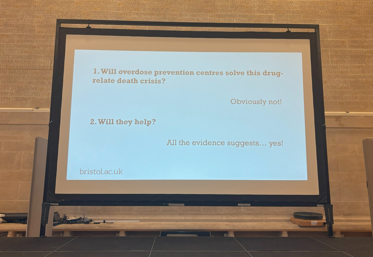 A slide from Dr Adam Hollands presentation, which details a conversation: 1. Will overdose prevention centres solve this drug-related death crisis? Answer- Obviously not! 2. Will they help? Answer- all the evidence suggests... yes!
